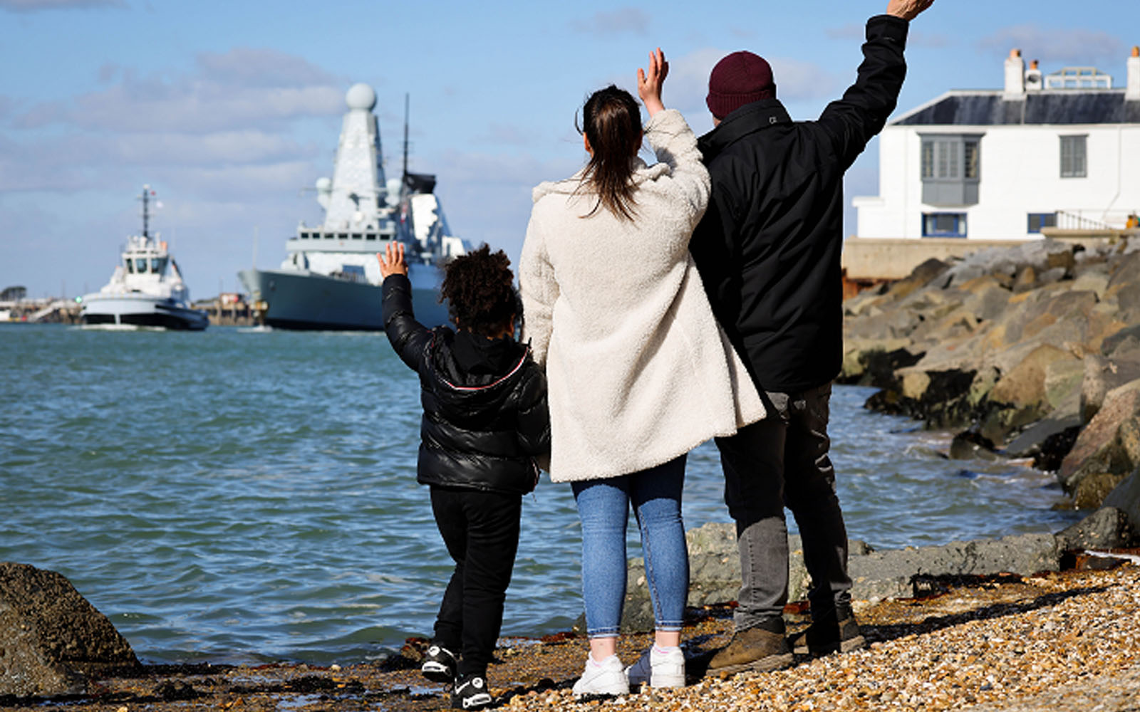 Three people on a shore waving at ships.
