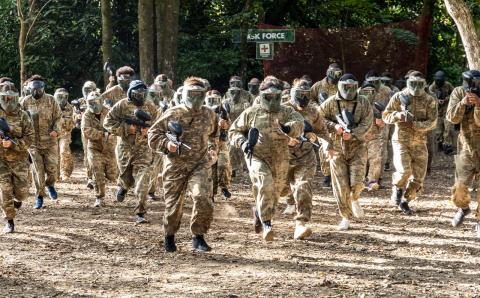 Wide shot of people in camouflage gear with paintball guns, in a forest.