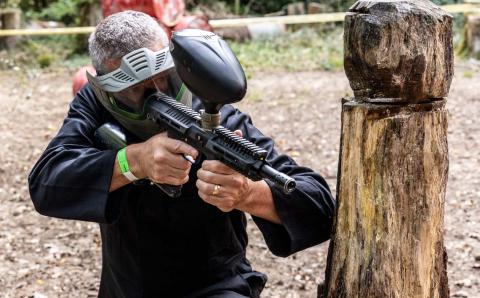 Close up of person holding a paintball gun, crouched behind a sculpture.