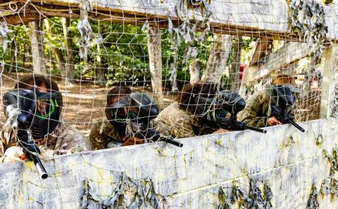 Four paintball participants crouched behind a wall.