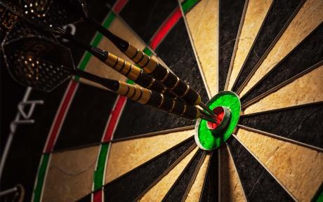 Close up of three darts in a bullseye on the dartboard.
