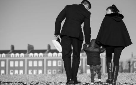 Serving navy person walking towards row of houses with family.