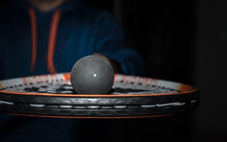 Close up of a squash ball on a racket.