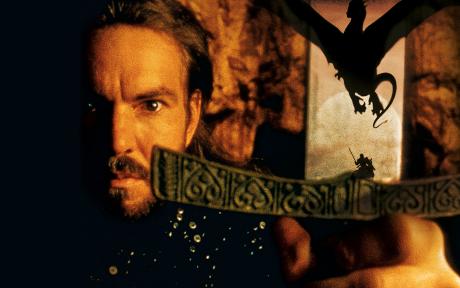 Movie still from the film Dragonheart. Close up of man holding a sword. Silhouette of a dragon behind him,