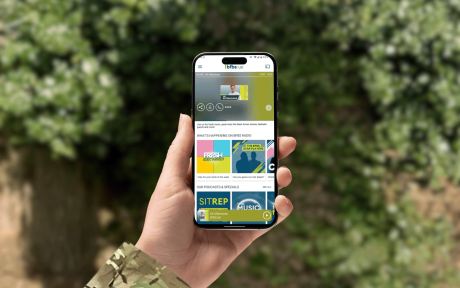 A hand holding a phone with the new BFBS Radio app on the screen.