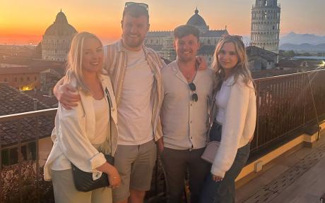 Group photo of two men and women on holiday, with the Italian city of Pisa in the background.