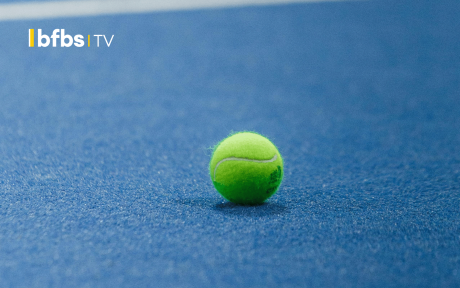 Tennis ball lying on a clay court.