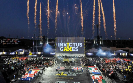 Wide shot of the a stadium, big screen with Invictus Games logo on, fireworks infront of a big crowd.